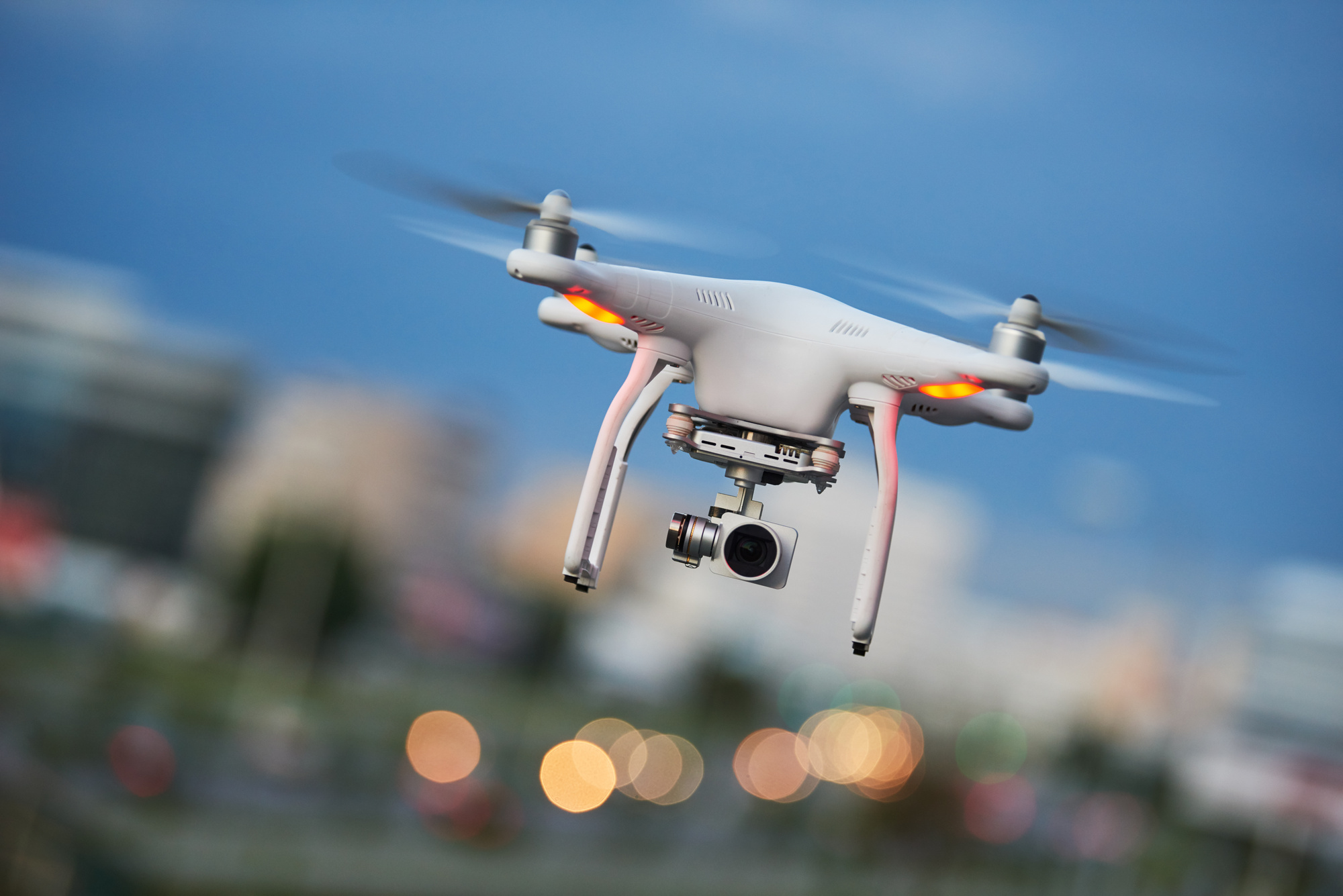 drone quadcopter with digital camera flying or hovering in evening blue sky over the city